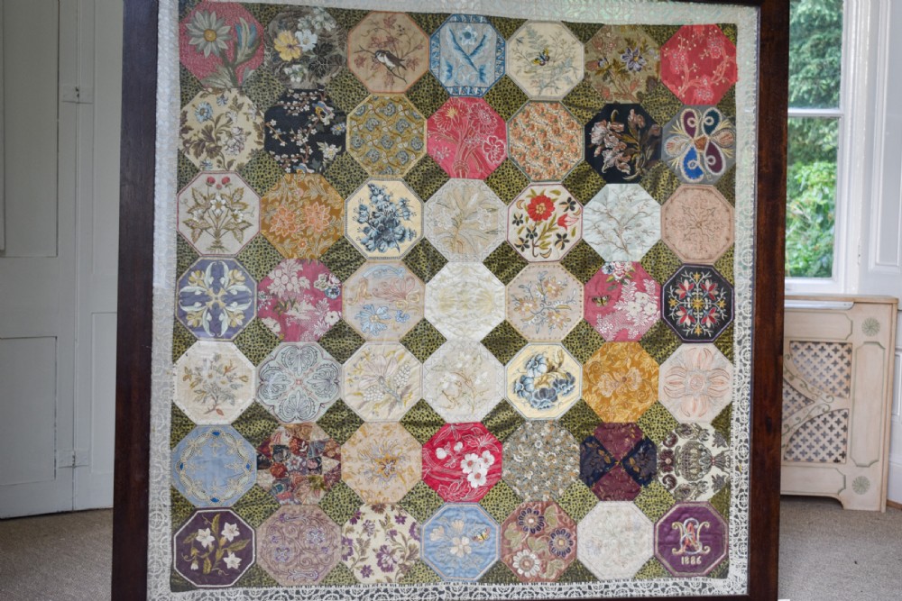 A large square framed Victorian silk patchwork panel featuring octagonal segments with intricate embroidered floral motifs and a dated section in the corner. View II