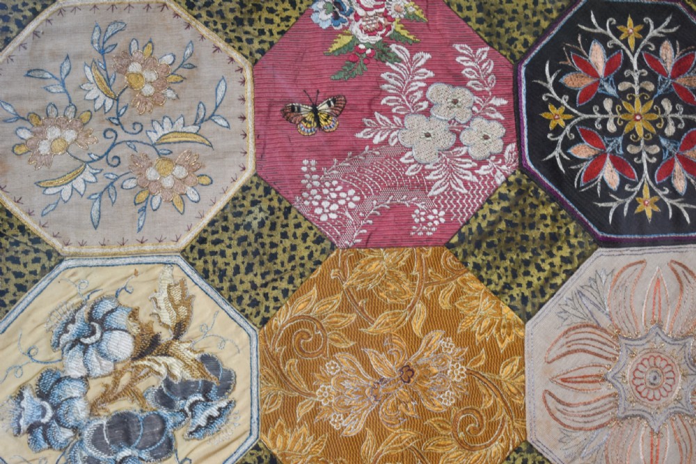 A large square framed Victorian silk patchwork panel featuring octagonal segments with intricate embroidered floral motifs and a dated section in the corner. View IV