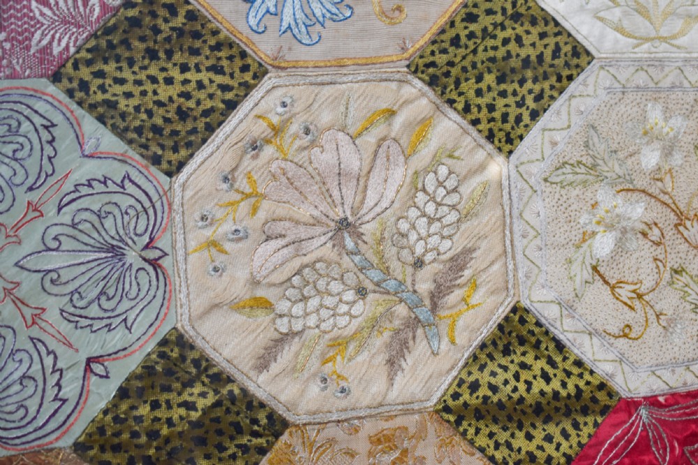 A large square framed Victorian silk patchwork panel featuring octagonal segments with intricate embroidered floral motifs and a dated section in the corner. View V