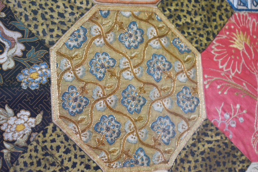 A large square framed Victorian silk patchwork panel featuring octagonal segments with intricate embroidered floral motifs and a dated section in the corner. View VI