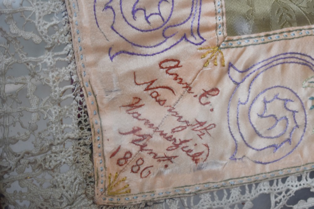 A large square framed Victorian silk patchwork panel featuring octagonal segments with intricate embroidered floral motifs and a dated section in the corner. View VIII