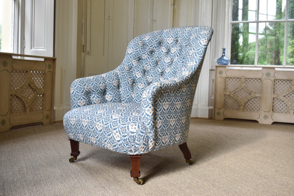 A deep Victorian button-back armchair upholstered in patterned blue and white fabric, set on turned mahogany front legs with brass castors.