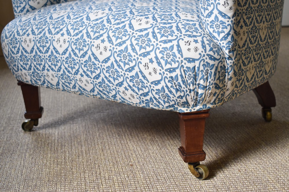 A deep Victorian button-back armchair upholstered in patterned blue and white fabric, set on turned mahogany front legs with brass castors. View III