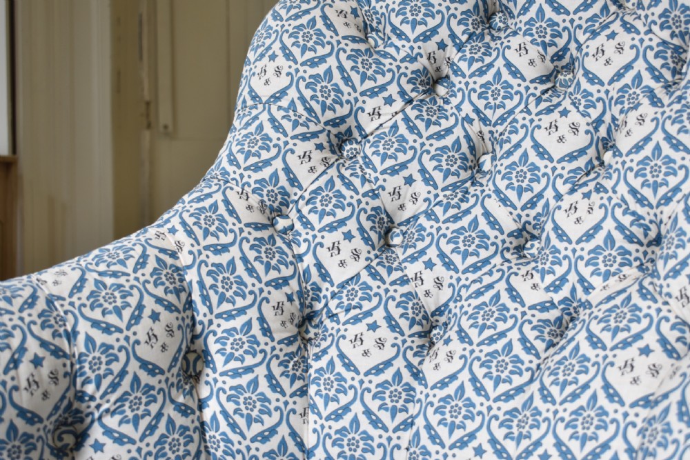 A deep Victorian button-back armchair upholstered in patterned blue and white fabric, set on turned mahogany front legs with brass castors. View IV