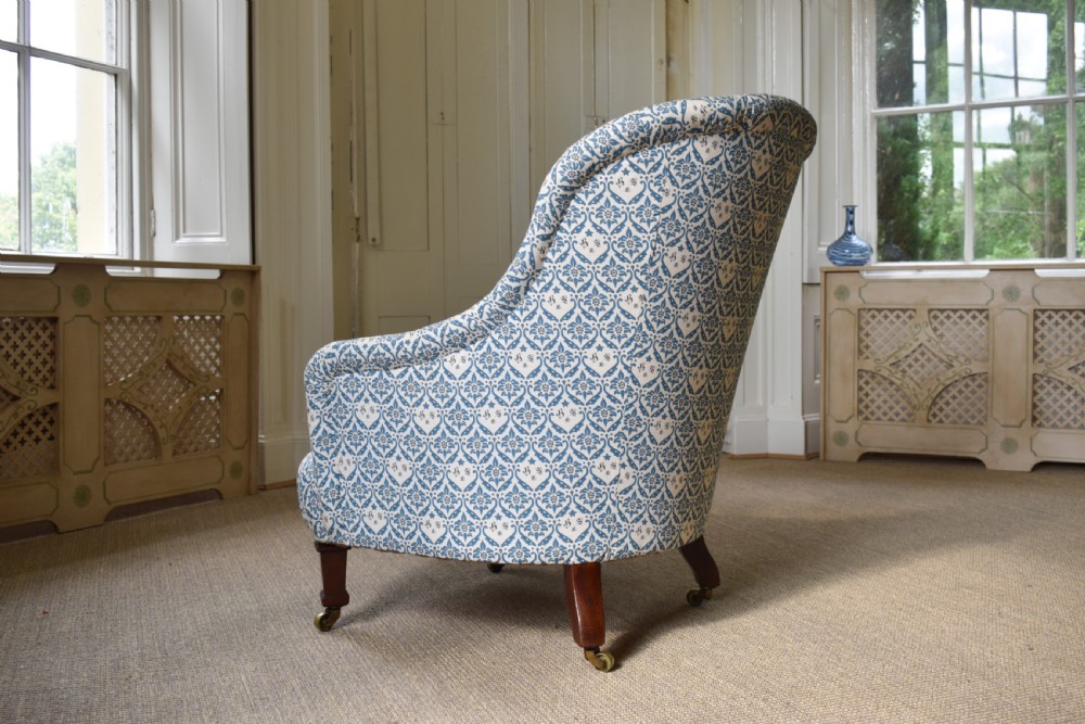 A deep Victorian button-back armchair upholstered in patterned blue and white fabric, set on turned mahogany front legs with brass castors. View V