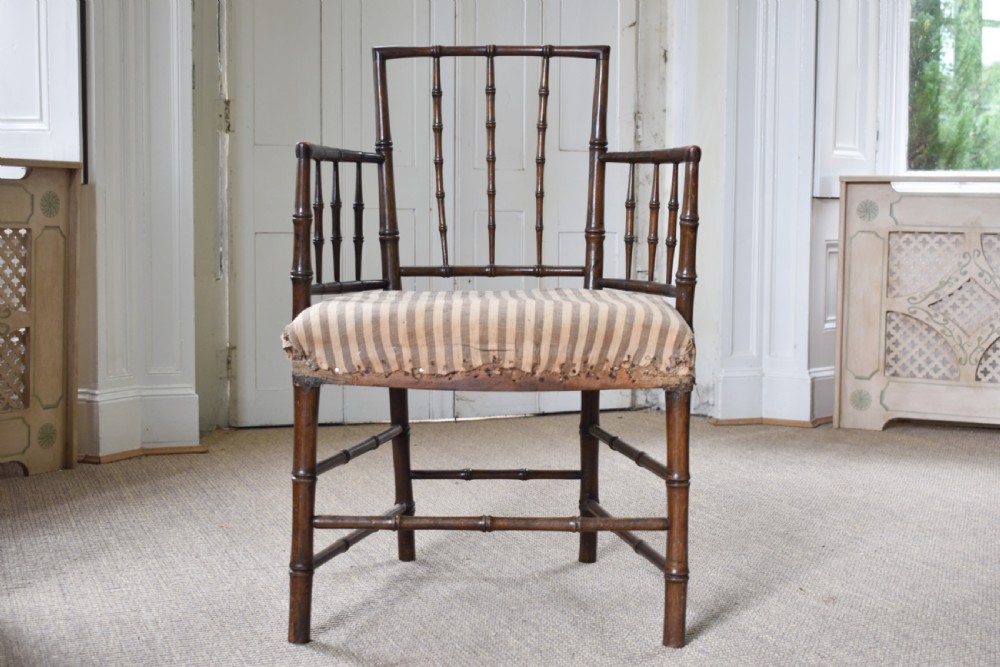 A dark-stained wooden armchair featuring simulated bamboo turnings across the frame and backrest, fitted with a striped fabric seat.