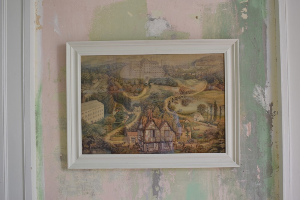 A framed watercolour painting featuring a detailed rural landscape with a brewery, timber-framed building, stone bridge, and rolling green hills. View II