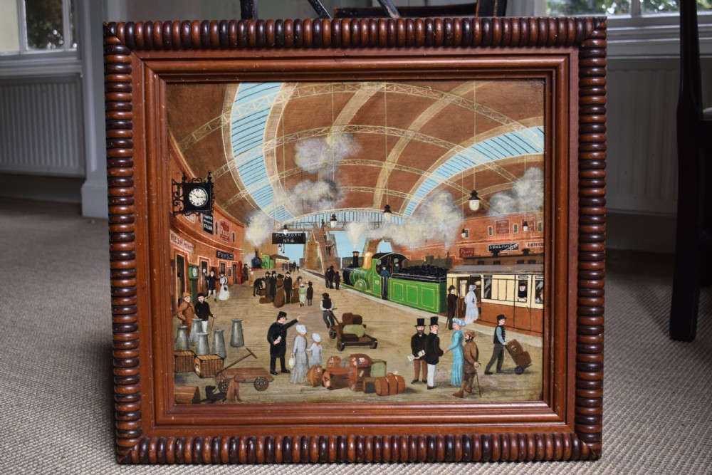 An oil painting on board depicting a busy Victorian steam train station scene inside a heavy bobbin-turned wood frame. View III