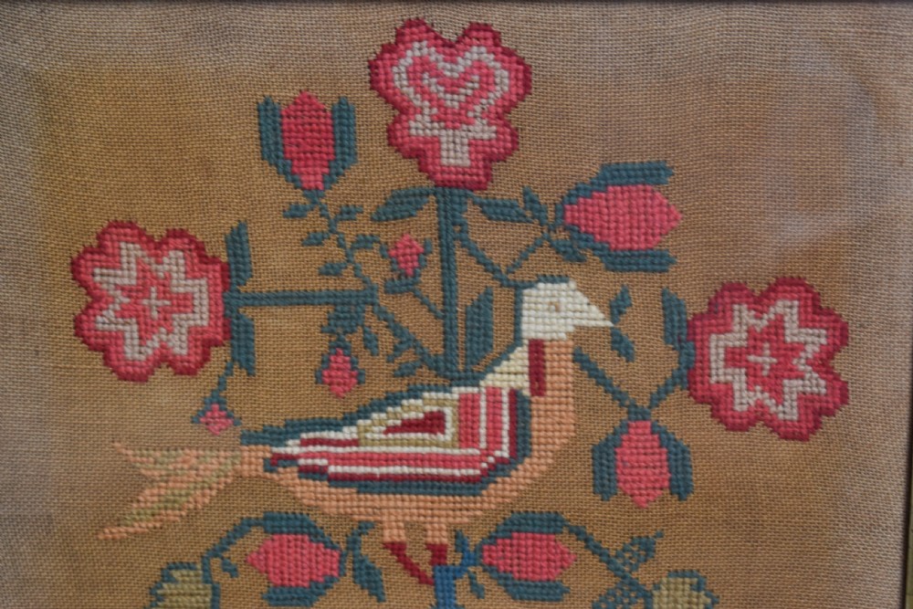 A framed 1844 Victorian needlework sampler featuring an embroidered bird perched on stylized floral stems with hearts and lettering, set in a dark wood frame. View II