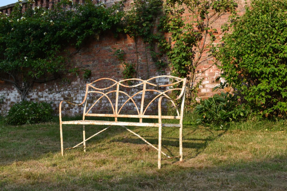 An antique off-white painted wrought iron garden bench featuring arched strapwork back panels and a weathered patina. View II