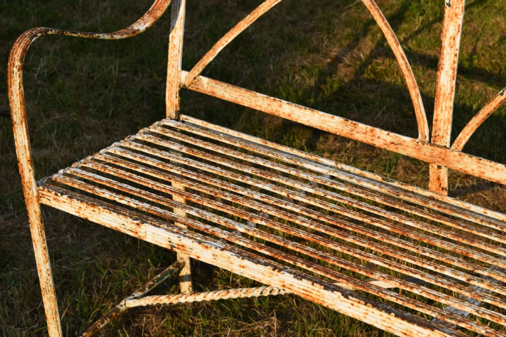 An antique off-white painted wrought iron garden bench featuring arched strapwork back panels and a weathered patina. View III