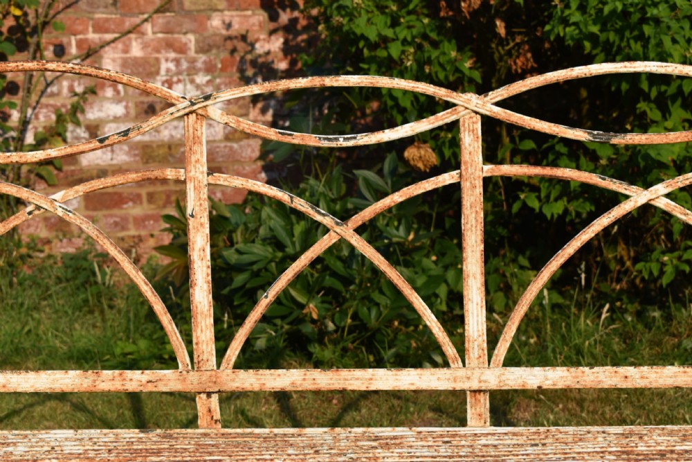 An antique off-white painted wrought iron garden bench featuring arched strapwork back panels and a weathered patina. View IV