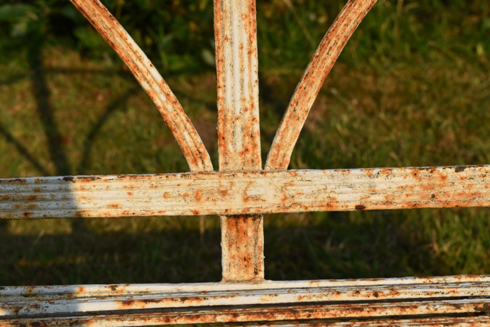 An antique off-white painted wrought iron garden bench featuring arched strapwork back panels and a weathered patina. View V