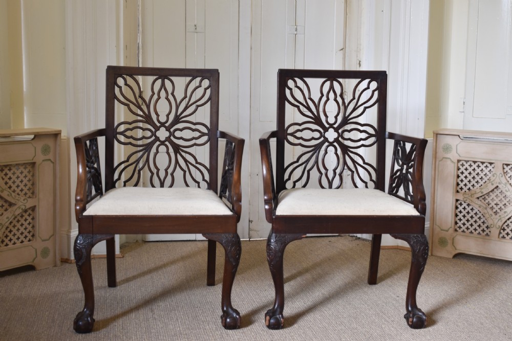 A pair of dark mahogany open armchairs featuring geometric floral fretwork backrests, open carved arms, cream upholstered seats, and cabriole legs with claw and ball feet. View VI