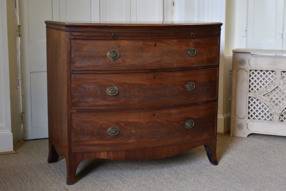 A Georgian flame mahogany bow-front chest of drawers with three open graduated drawers and circular brass handles. View II