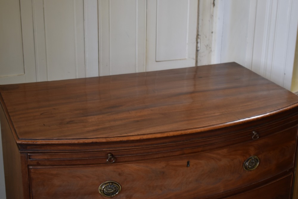 A Georgian flame mahogany bow-front chest of drawers with three open graduated drawers and circular brass handles. View IV