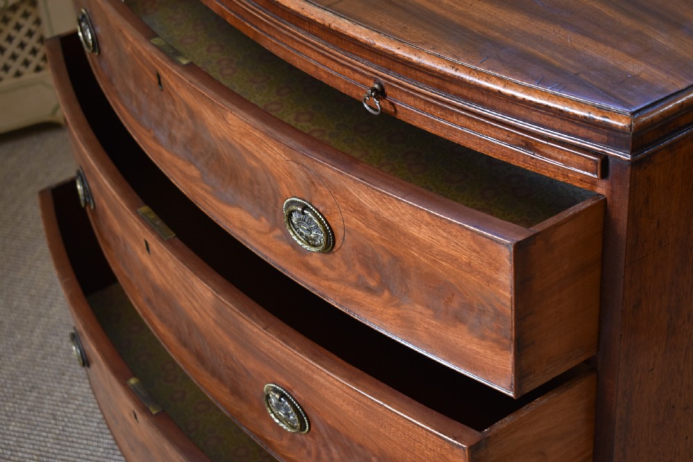 A Georgian flame mahogany bow-front chest of drawers with three open graduated drawers and circular brass handles. View VI