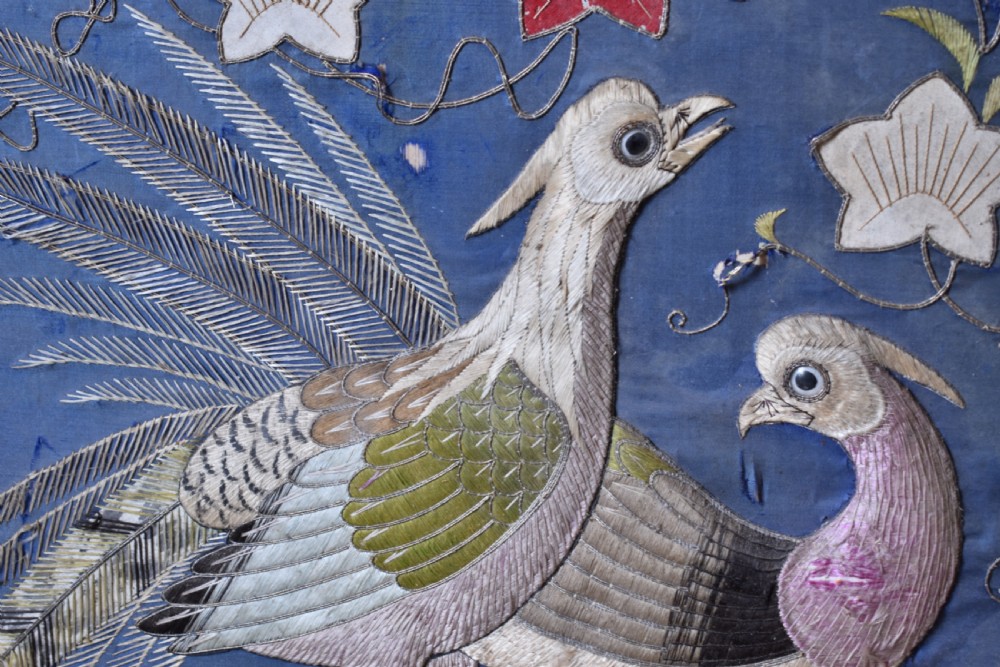 A square framed textile picture featuring two embroidered birds surrounded by floral motifs on a blue silk ground. View II