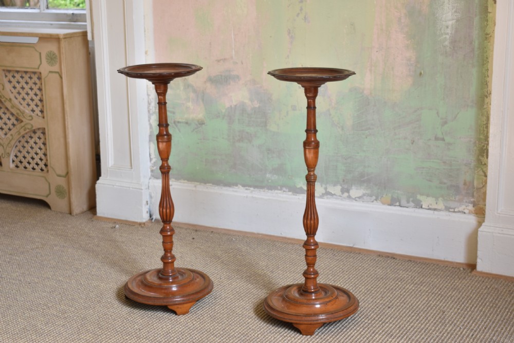 A pair of tall, slender antique satinwood candle stands featuring circular tray tops, fluted turned columns, and circular molded bases.