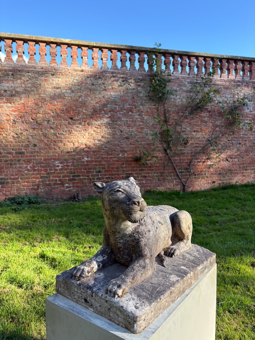 A carved marble sculpture depicting a recumbent lioness resting on an integral rectangular stone base. View III