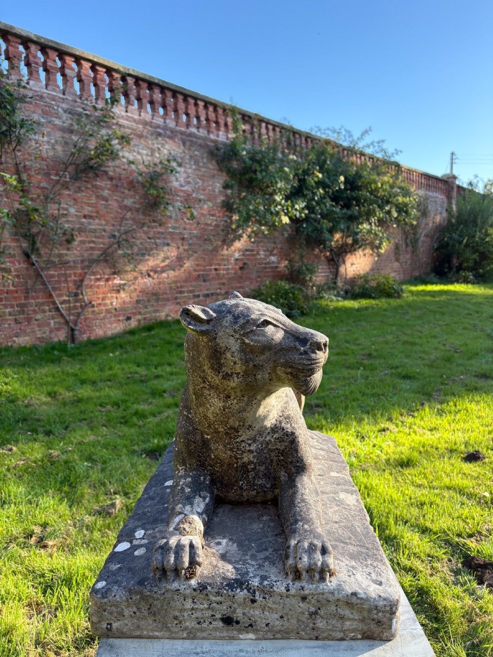 A carved marble sculpture depicting a recumbent lioness resting on an integral rectangular stone base. View IV