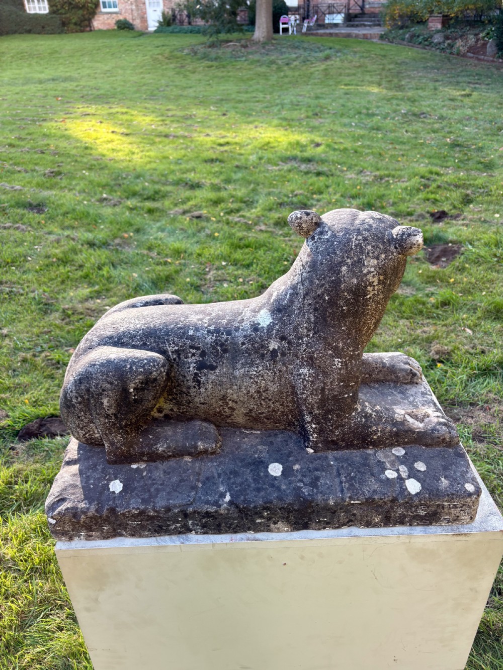 A carved marble sculpture depicting a recumbent lioness resting on an integral rectangular stone base. View V