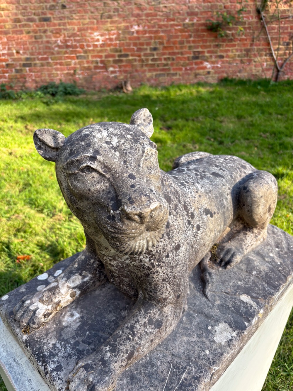 A carved marble sculpture depicting a recumbent lioness resting on an integral rectangular stone base. View VI