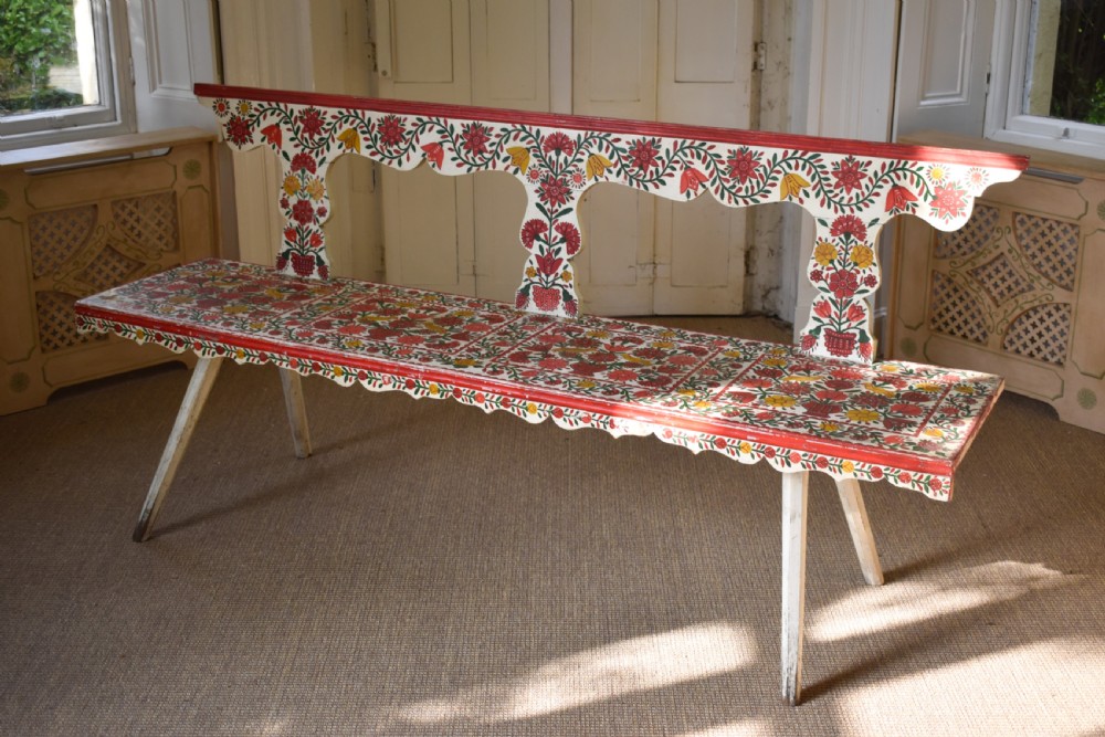 A long hand-painted wooden bench decorated with red, yellow, and green floral patterns across its seat, scalloped backrest, and front apron.