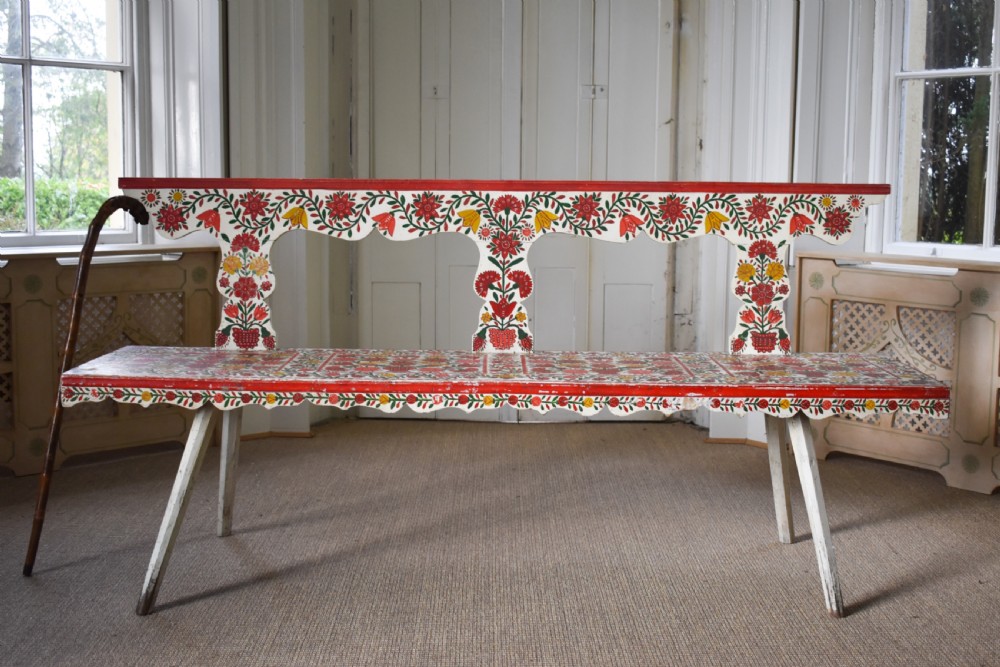 A long hand-painted wooden bench decorated with red, yellow, and green floral patterns across its seat, scalloped backrest, and front apron. View IV