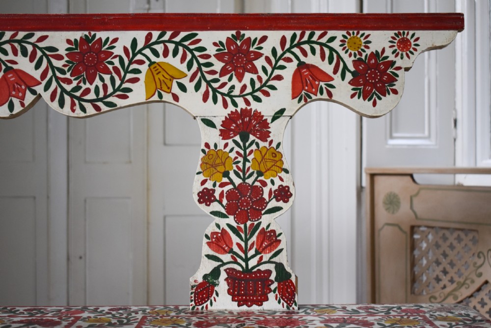 A long hand-painted wooden bench decorated with red, yellow, and green floral patterns across its seat, scalloped backrest, and front apron. View V