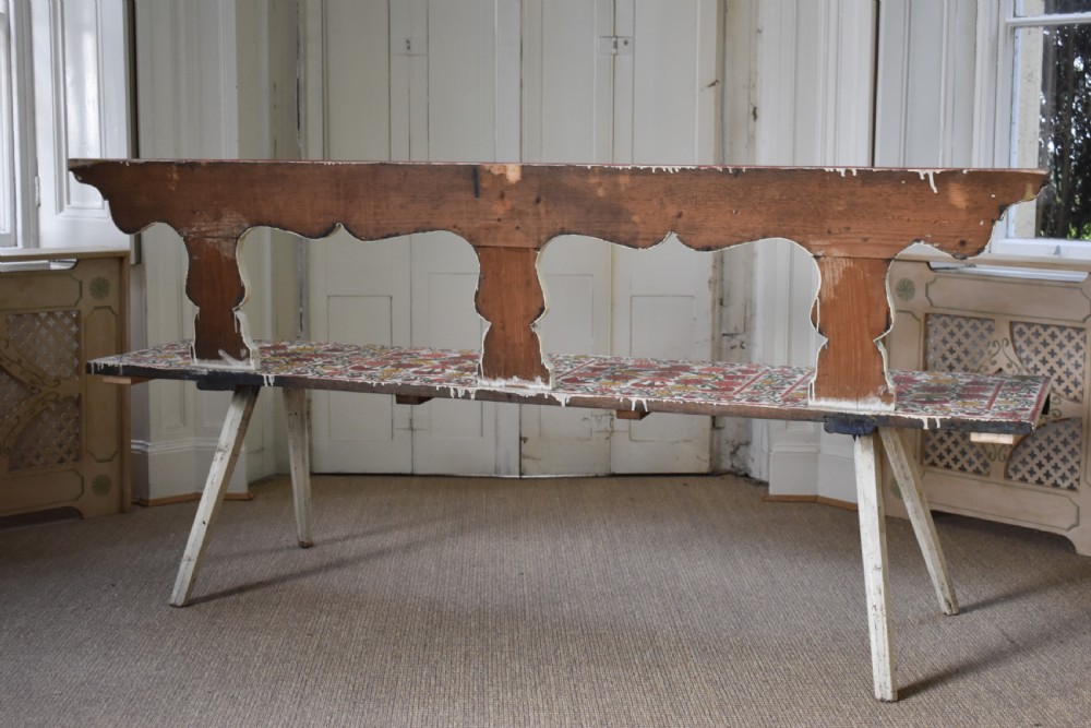 A long hand-painted wooden bench decorated with red, yellow, and green floral patterns across its seat, scalloped backrest, and front apron. View VII