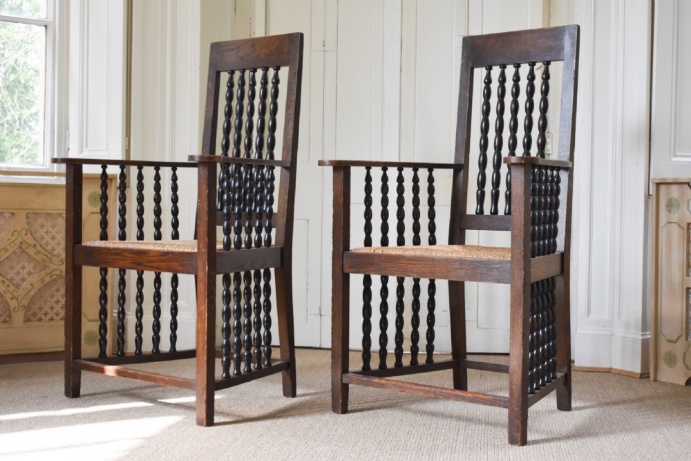 A pair of dark oak high-backed armchairs featuring bobbin-turned spindle backs, open arms with spindle supports, and woven rush seats.