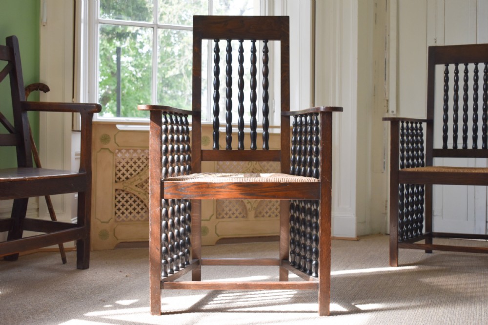 A pair of dark oak high-backed armchairs featuring bobbin-turned spindle backs, open arms with spindle supports, and woven rush seats. View II