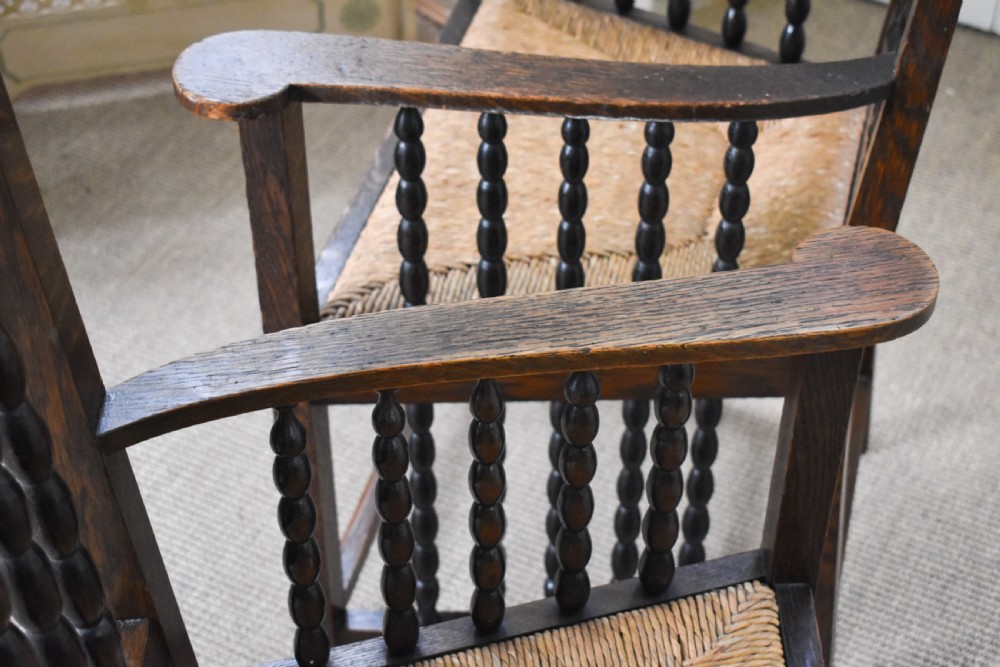 A pair of dark oak high-backed armchairs featuring bobbin-turned spindle backs, open arms with spindle supports, and woven rush seats. View V