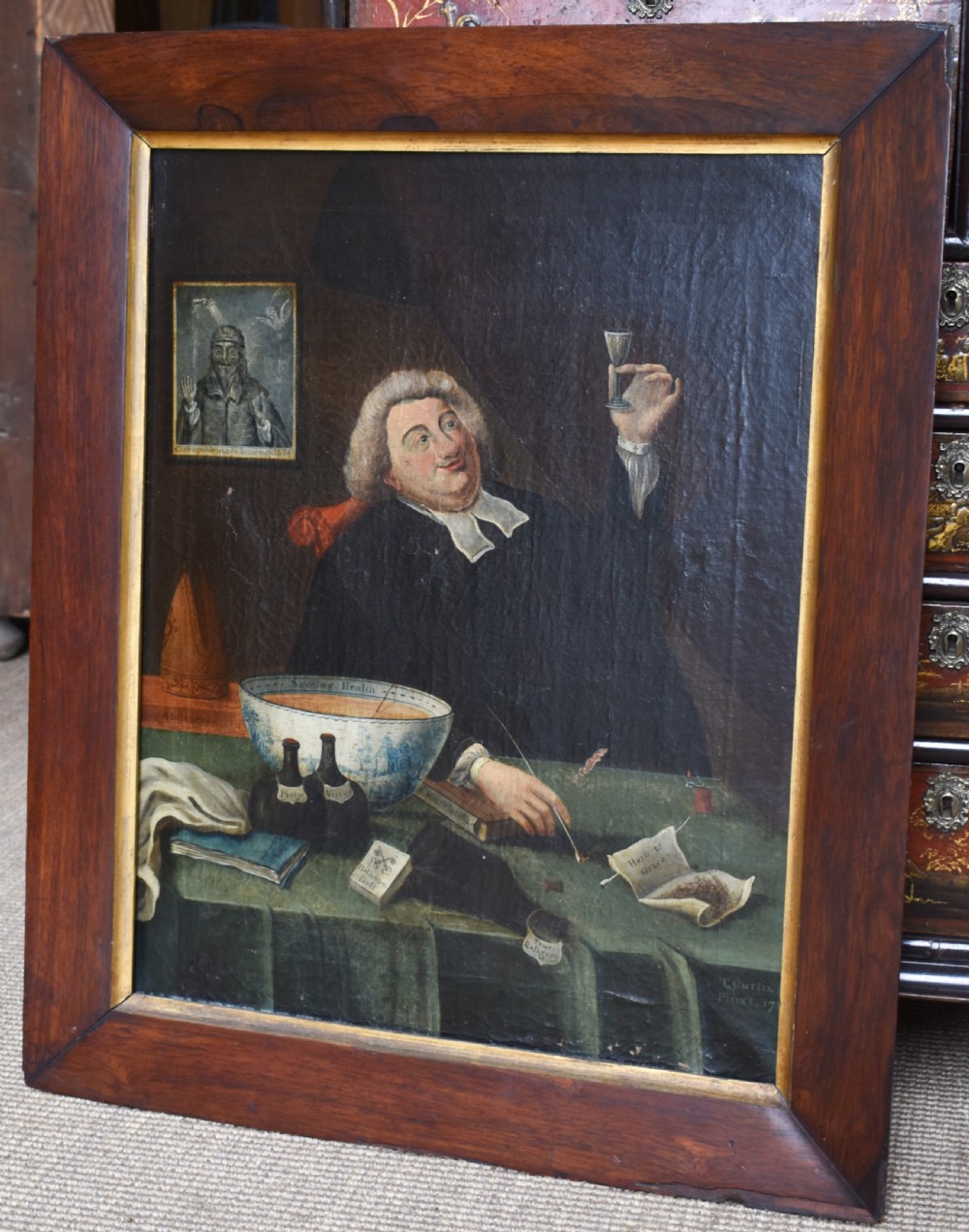 An eighteenth-century oil painting depicting a clergyman seated at a draped table with a punch bowl and glass, encased in a dark wooden frame with a gilded inner slip.