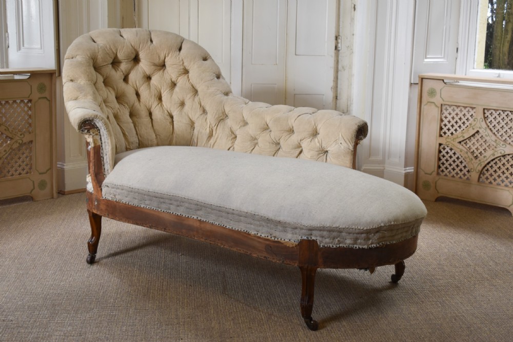 A Victorian upholstered chaise longue with deep-buttoned backrest, carved mahogany frame, and castors on cabriole legs.