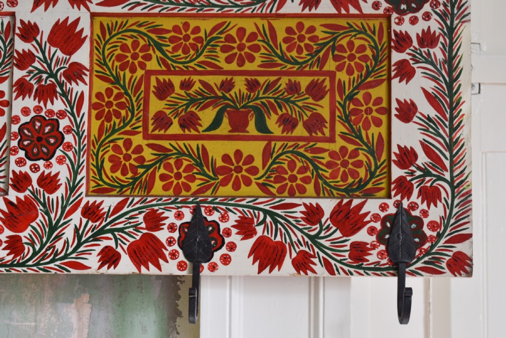 A long wall-mounted wooden coat rack featuring hand-painted red and yellow floral folk art patterns, a scalloped top edge, and eight iron hooks. View II