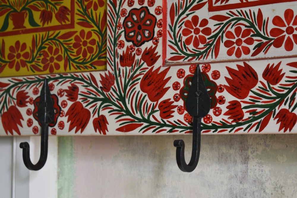 A long wall-mounted wooden coat rack featuring hand-painted red and yellow floral folk art patterns, a scalloped top edge, and eight iron hooks. View III