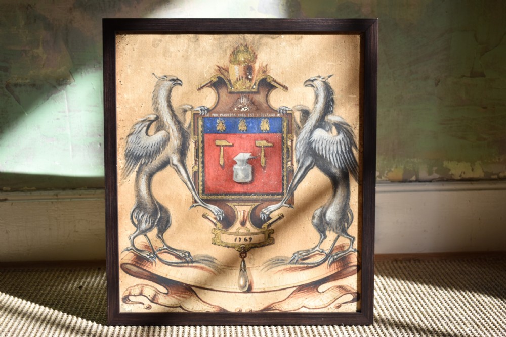 A framed 18th-century heraldic artwork displaying a central coat of arms with anvil motifs flanked by two heraldic griffin supporters.