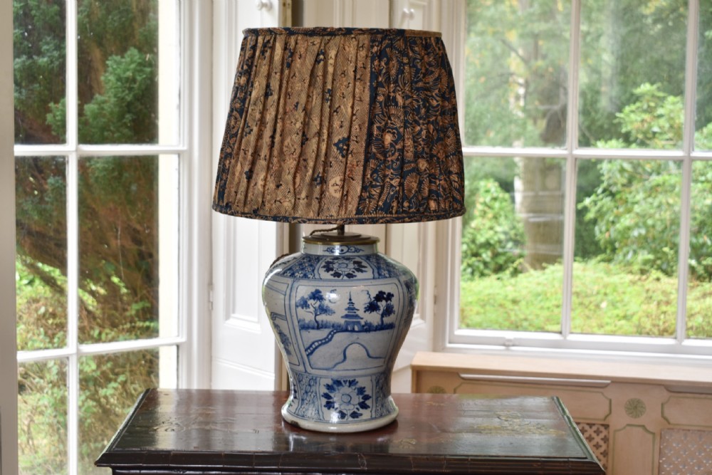 A Chinese blue and white ceramic baluster vase fitted as a table lamp with a navy and gold pleated patterned fabric shade.