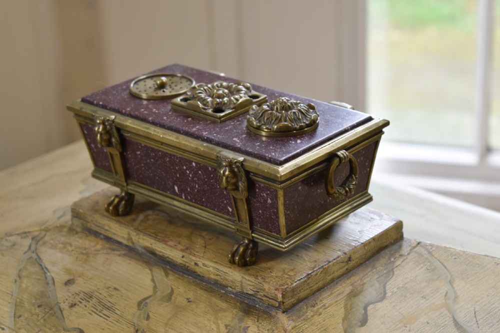 A Regency period sarcophagus-form porphyry inkstand with gilt bronze lion feet, side drop handles, and brass inkwell covers.