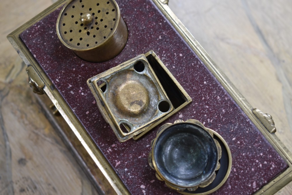A Regency period sarcophagus-form porphyry inkstand with gilt bronze lion feet, side drop handles, and brass inkwell covers. View V