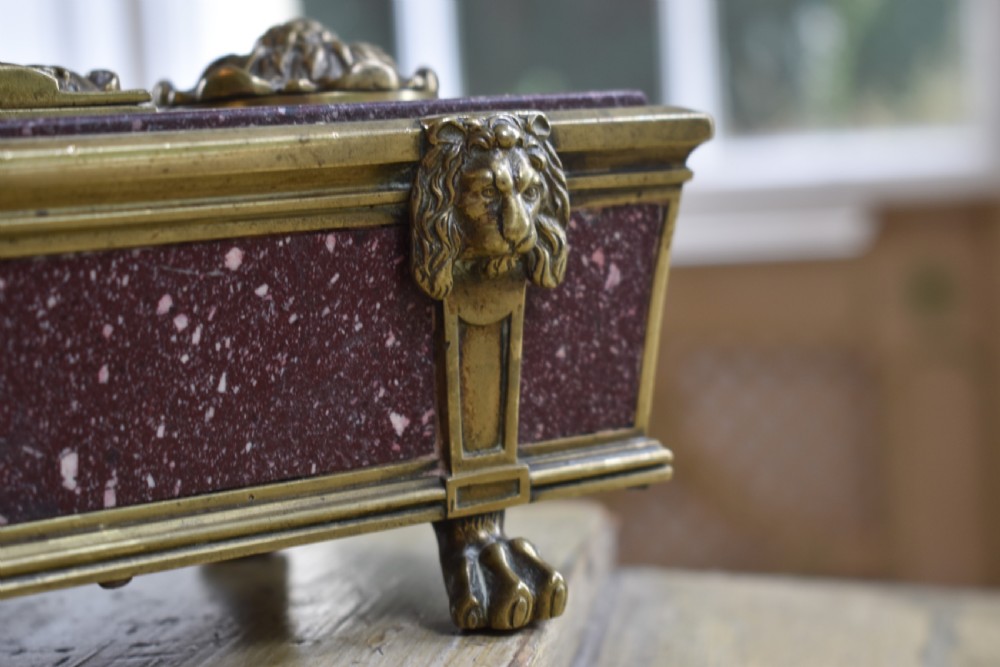 A Regency period sarcophagus-form porphyry inkstand with gilt bronze lion feet, side drop handles, and brass inkwell covers. View VII