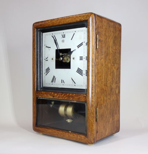 fig 1. An Art Deco oak-cased mantel clock featuring a square white dial with Roman numerals and a clear glass window revealing the brass pendulum mechanism below.