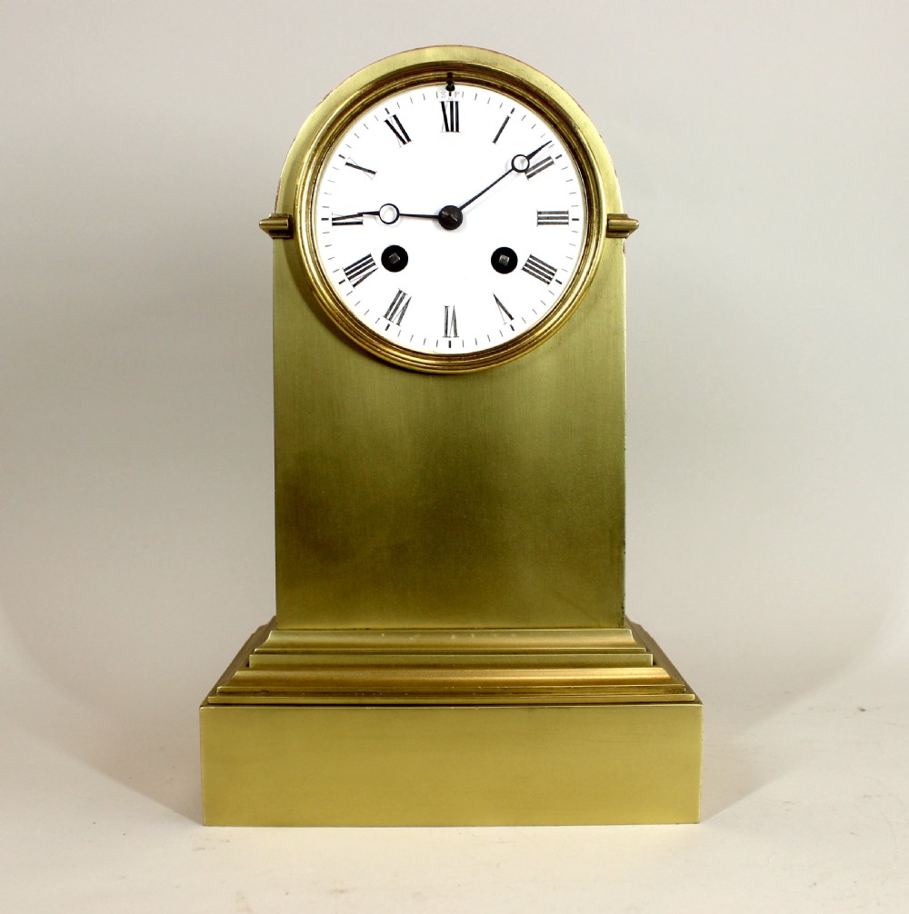 A polished brass dome-topped mantel clock featuring a white enamel dial with Roman numerals on a stepped rectangular base.