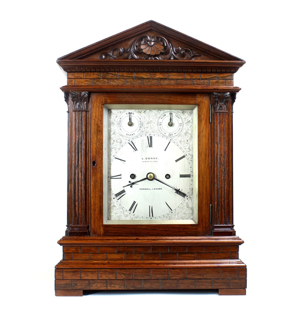 An antique rosewood architectural bracket clock featuring a pediment roof with a carved shell motif, fluted columns, and an engraved silvered dial with Roman numerals.