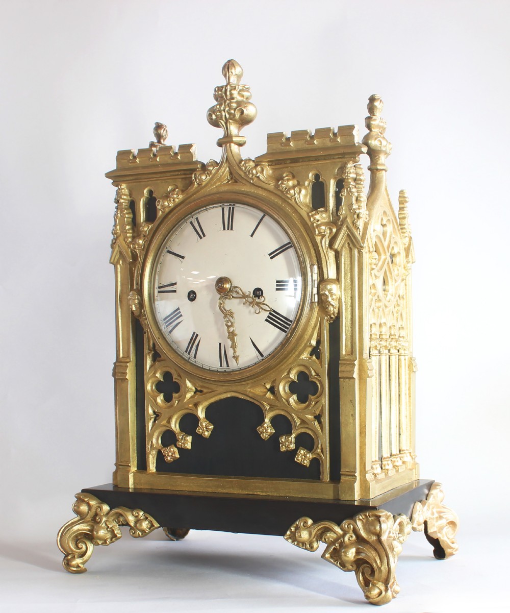A Gothic Revival gilt brass and bronze mantel clock featuring architectural tracery, pointed arches, a white enamel dial with Roman numerals, and scroll feet. View II