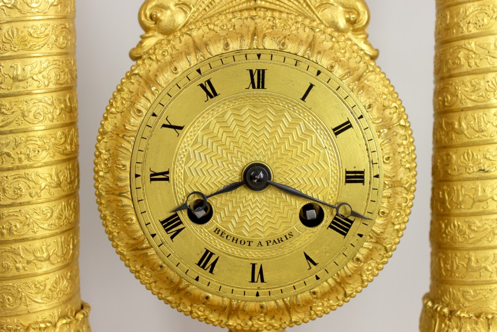 An antique French Empire style gilt bronze portico mystery clock featuring detailed columns supporting a decorated top frieze and suspending a circular dial with a gridiron pendulum. View VII