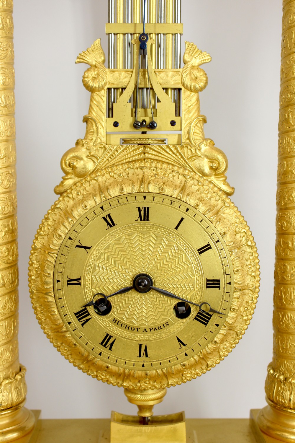 An antique French Empire style gilt bronze portico mystery clock featuring detailed columns supporting a decorated top frieze and suspending a circular dial with a gridiron pendulum. View VIII