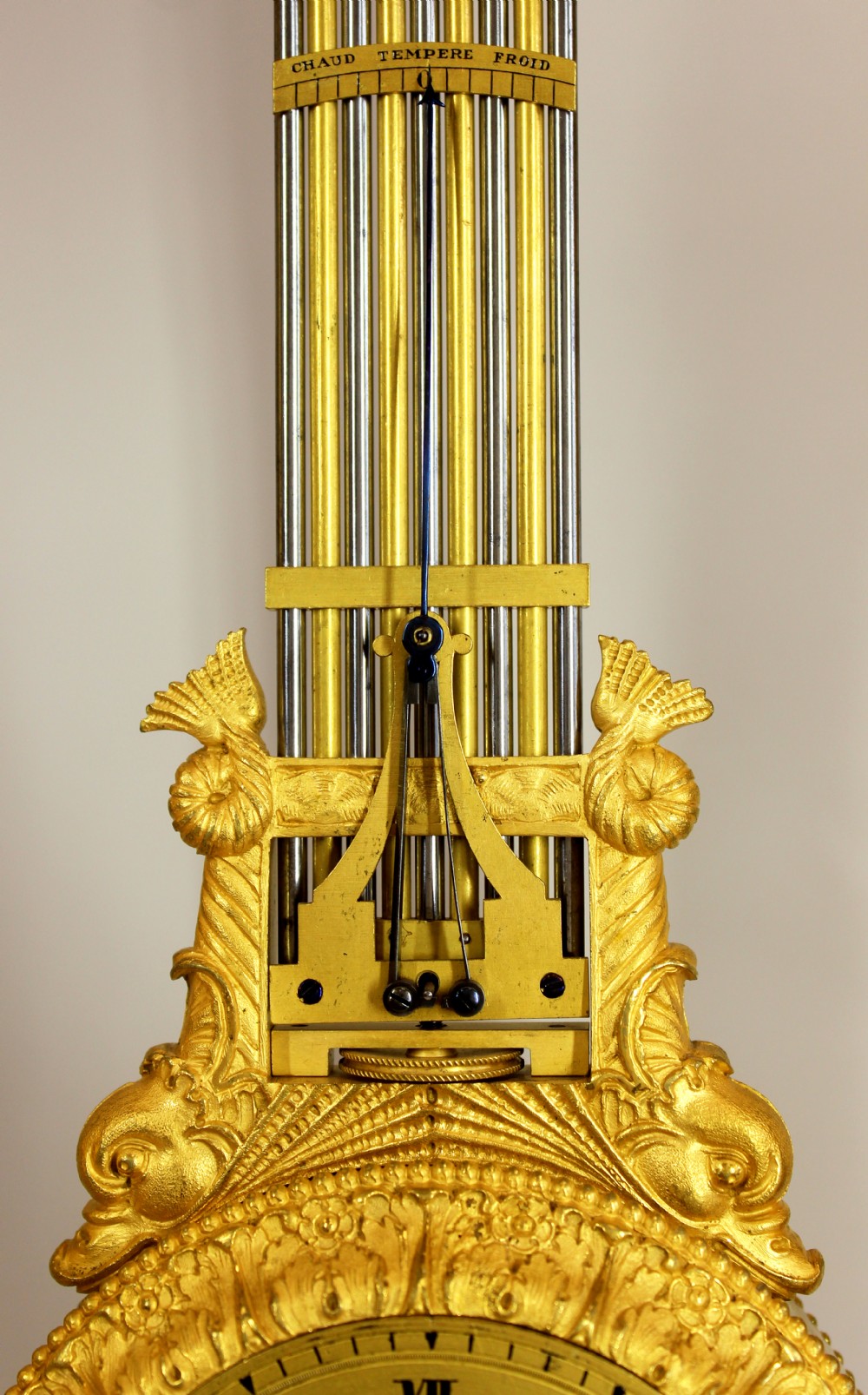 An antique French Empire style gilt bronze portico mystery clock featuring detailed columns supporting a decorated top frieze and suspending a circular dial with a gridiron pendulum. View IX